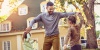 Man dancing with two children in the yard of a home.